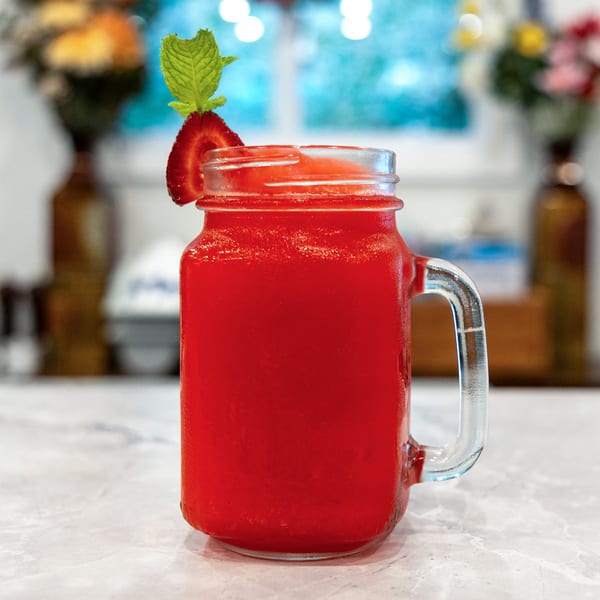 Bright red strawberry drink served in a glass mason jar, garnished with a strawberry slice and fresh mint.