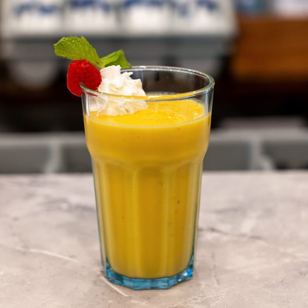 Yellow smoothie in a glass topped with whipped cream, raspberry, and fresh mint on a restaurant counter.