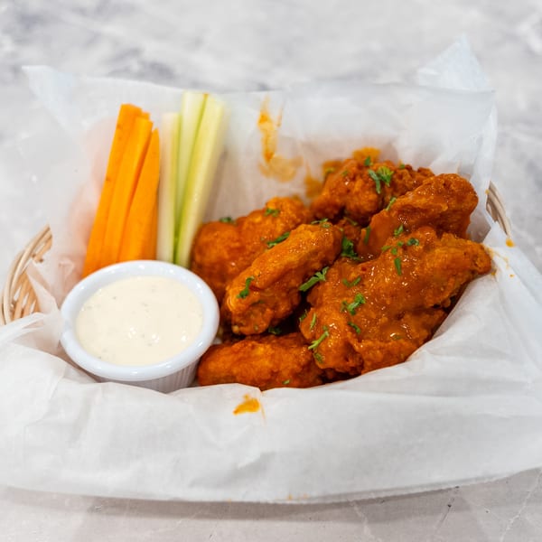 Basket of saucy buffalo chicken wings garnished with herbs, served with carrot and celery sticks and creamy dipping sauce.